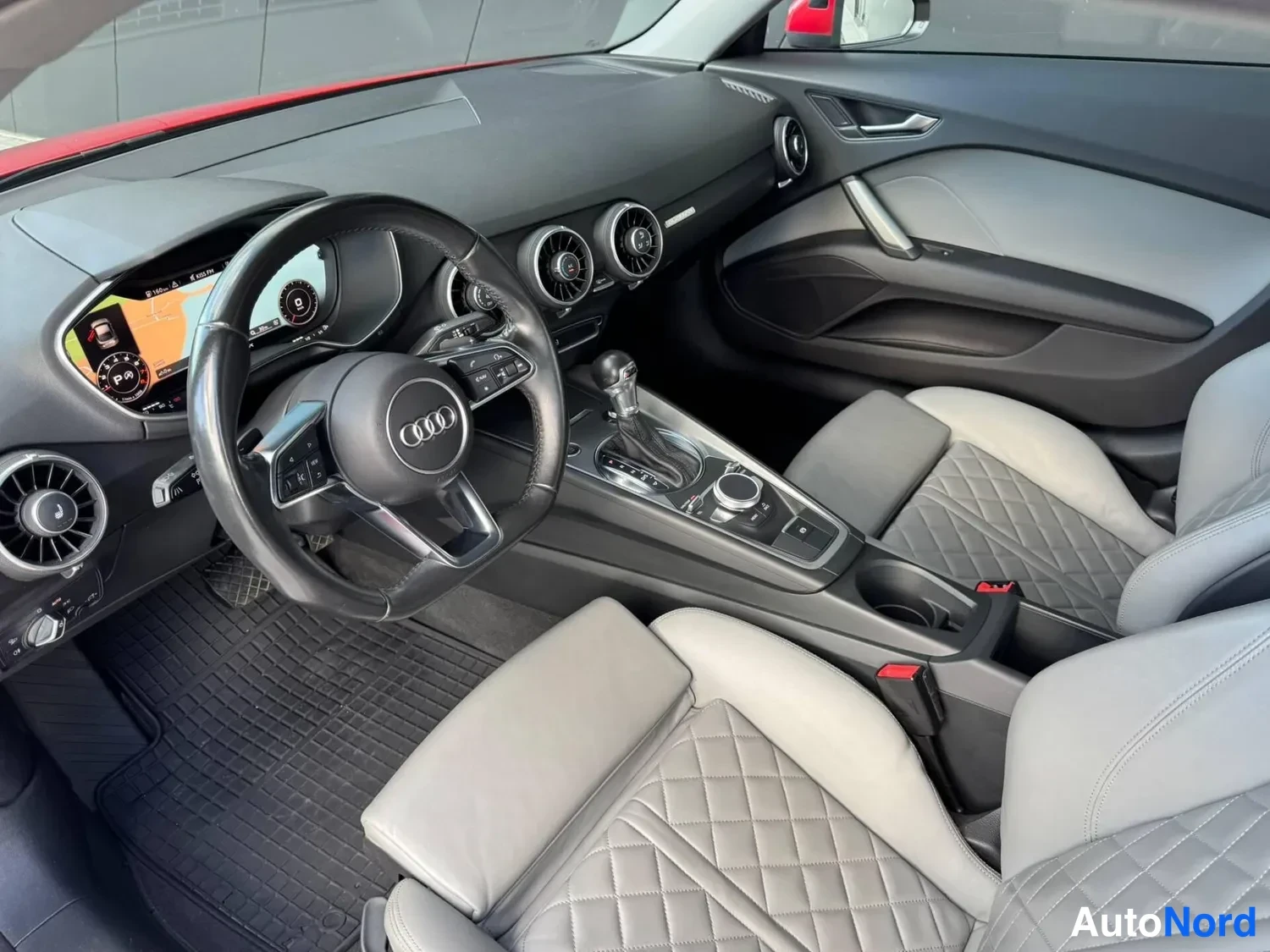 Sivulta: Audi TT:n sisätilat: ohjauspyörä, mittaristo, ilmastointiautomaatti ja kahteen istuinrivin keskikäytävä kuljettajan puolelta kuvattuna.