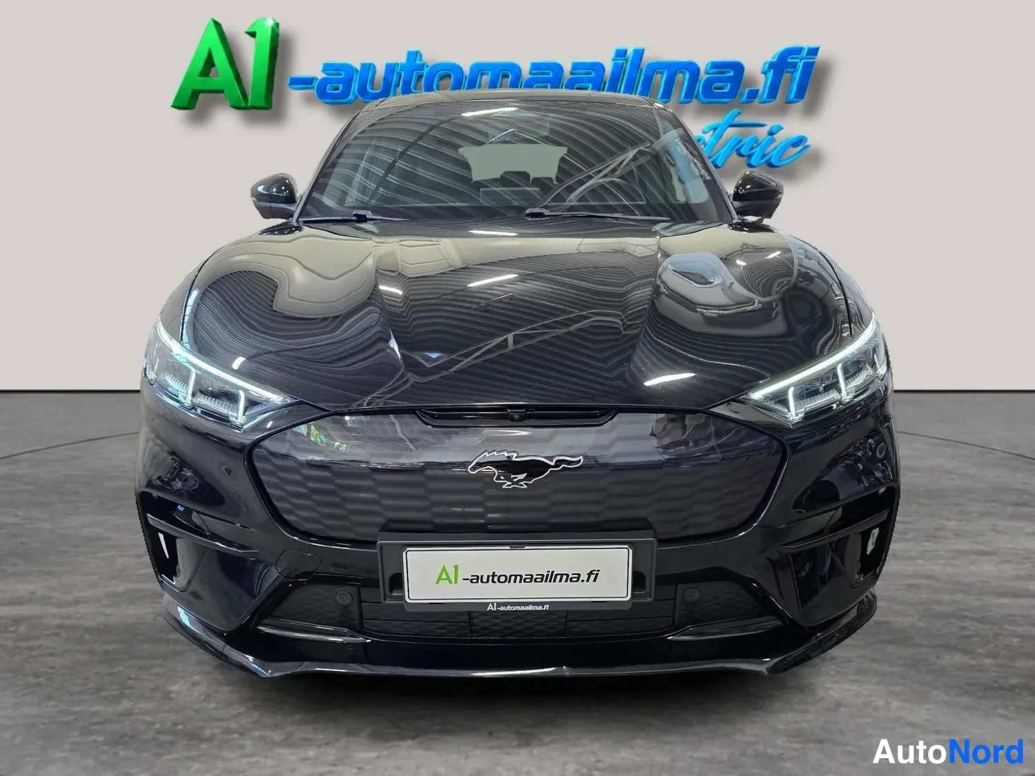 Edestä: Musta Ford Mustang Mach-E suoraan edestä,イルmajohtuvat ajovalot ja Pony-merkki etusäleikössä.