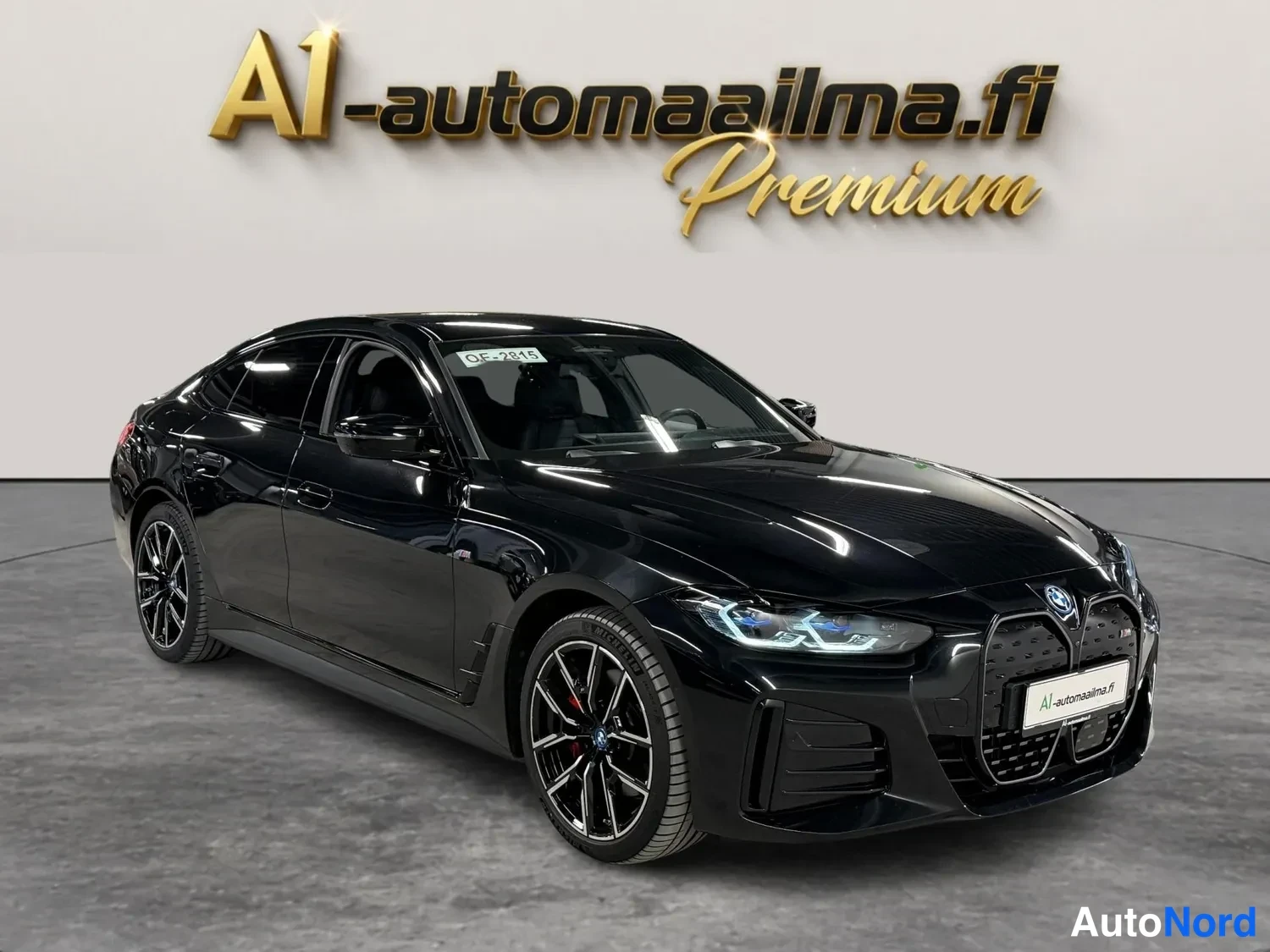 Etuviisto, nokka oikealle: Mustan BMW i4:n etukolmäsivukuva näyttää etusäleikön, LED-ajovalot ja mustat kevytmetallivanteet, joiden takana punaiset jarrusatulat.