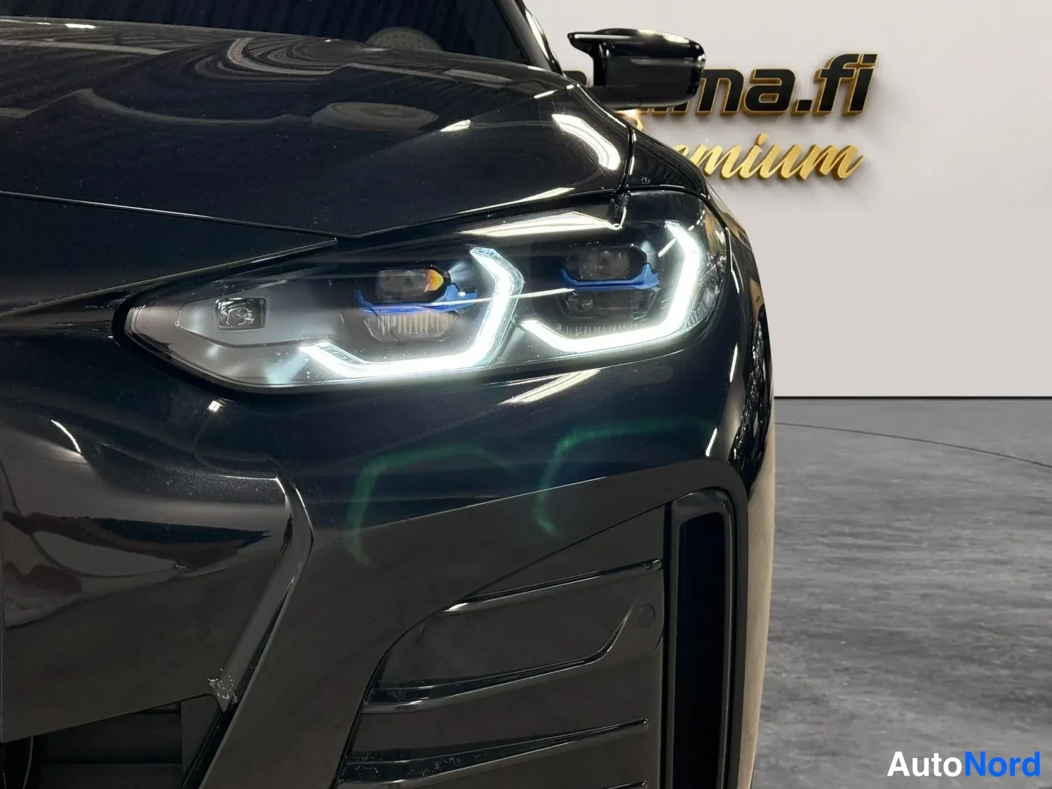 Edestä: Mustan auton etuosan lähikuva: sytytetty LED-etuvalo, musta konepelti ja etupuskurin ilmanottoaukko sisätiloissa.
