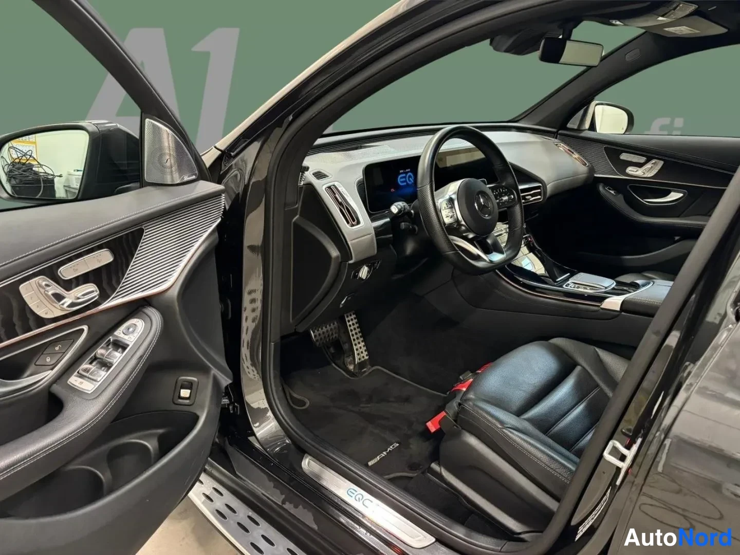 Muu: Mercedes-Benzin ohjaamo kuljettajan ovi auki: nahkaverhoillut penkit, AMG-ovenkynnäksellä teksti EQC, tallautin ja elektroninen mittaristo.
