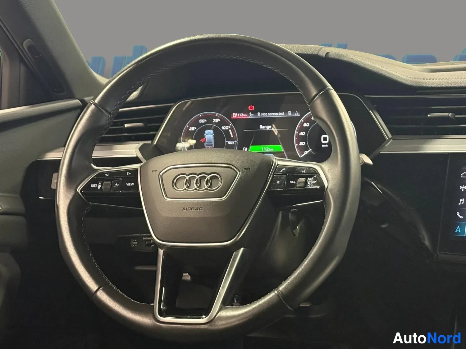 Muu: Audi-ohjauspyörä lähikuvassa AIRBAG-tekstillä; mittaristo näyttää Range-tilan ja 112 km toimintamatkan.