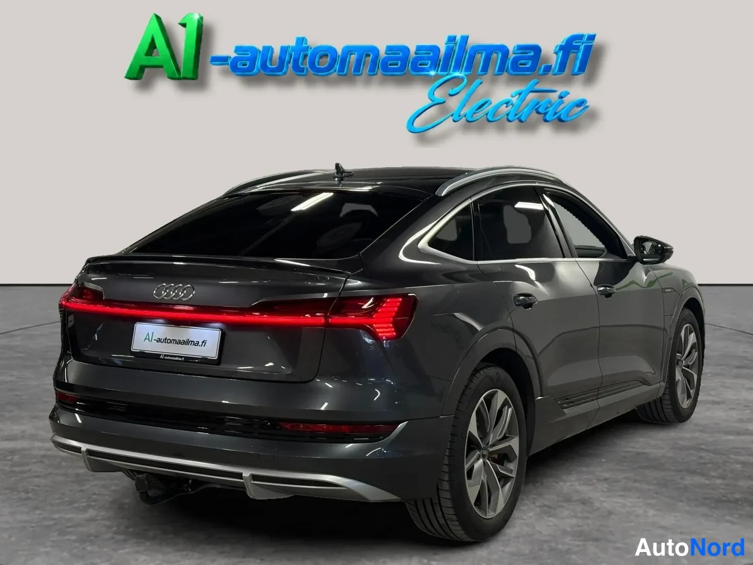 Takaviisto: Takavasemmalta kolmasosa -näkymä tummanharmaasta Audi Sportback -mallista, jossa näkyvät takavalot, takapuskuri ja sivuovet.