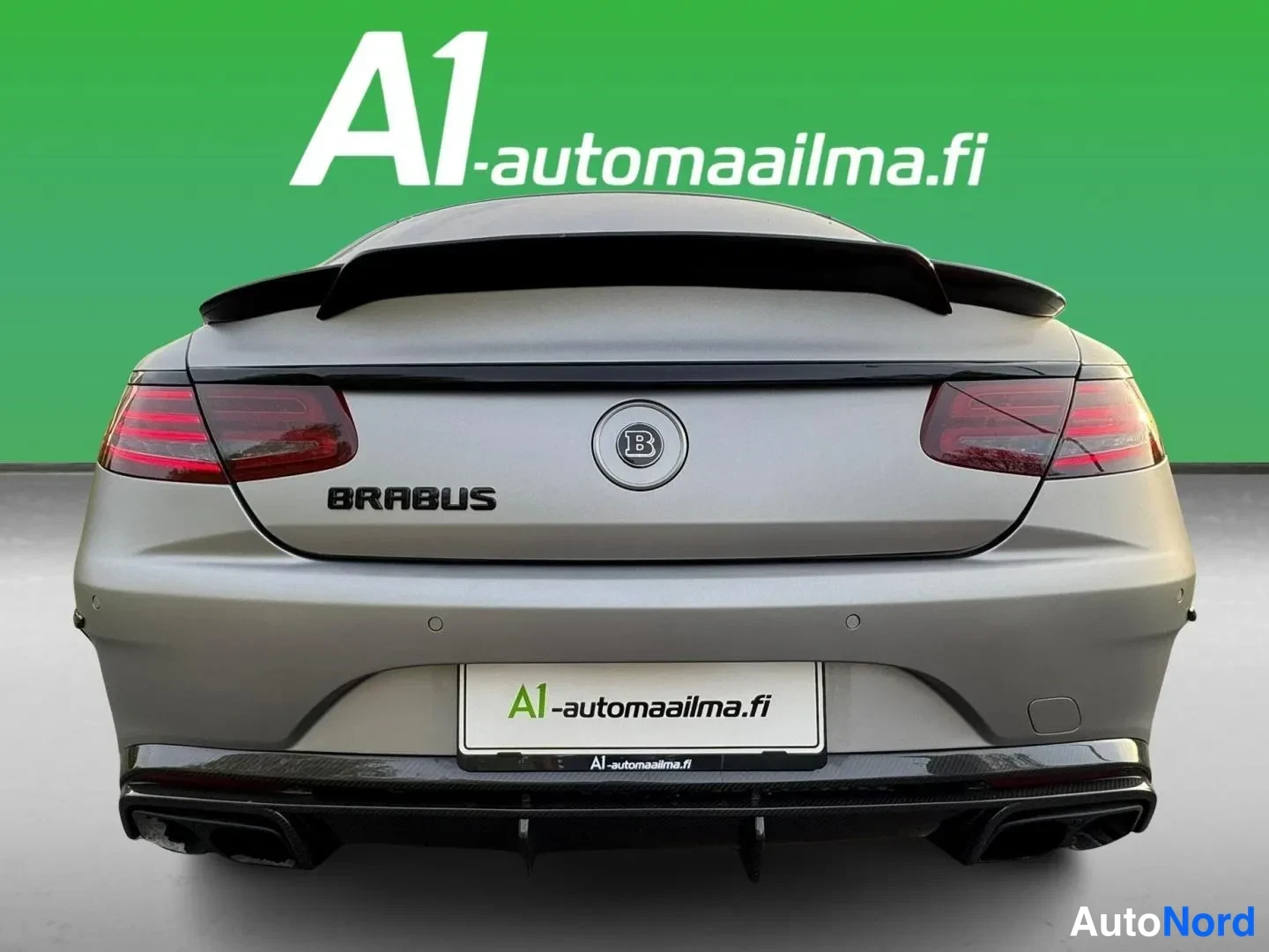 Takaa: Auton suora takaosa; BRABUS-teksti takaluukussa, B-tunnuksella, musta spoileri ja musta puskurin alaosa.