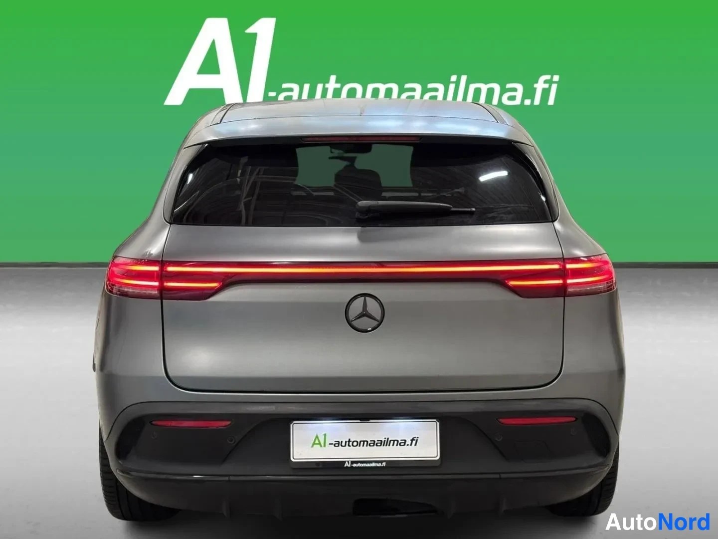 Takaa: Auton takaosa suoraan takaa: Mercedes-tähti, poikittain kulkeva punainen takavalojensarja ja perävaunukytkimen alusrakenne harmaalla korilla.
