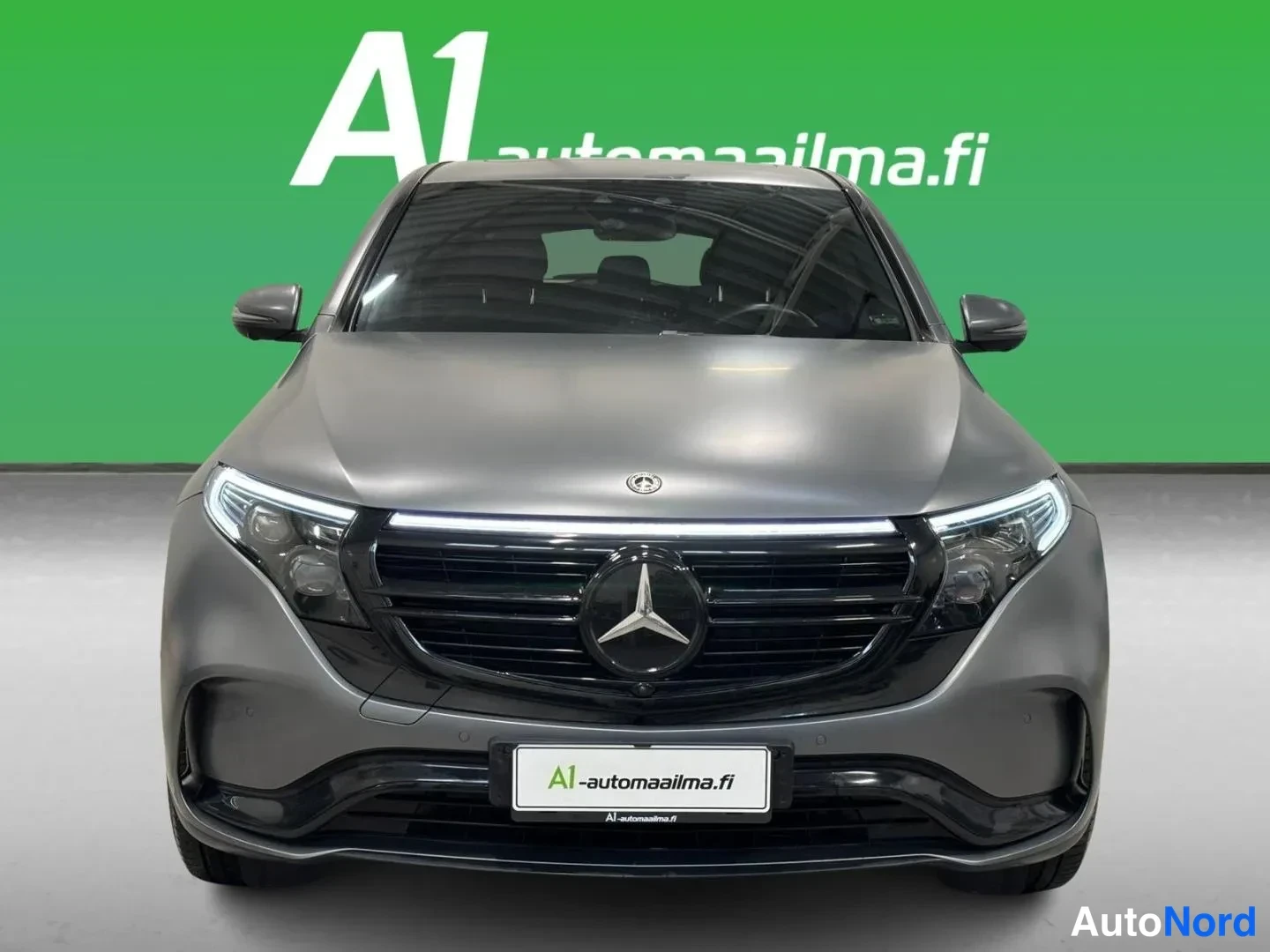 Edestä: Mercedes-Benz EQC:n etupää suoraan edestä; harmaa kori, merkkivalot ja A1-automaailma-tunniste.