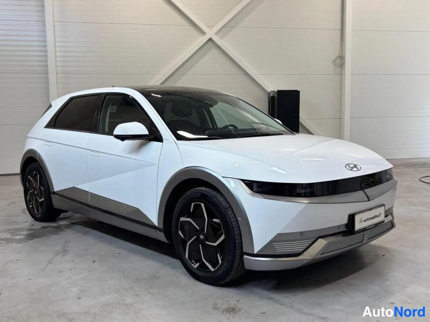Etuviisto, nokka oikealle: Valkoinen Hyundai Ioniq 5 etuvasemmalta kolmeneljäsosakulmasta kuvattuna hallissa, tummat ikkunat ja tummat vanteet.