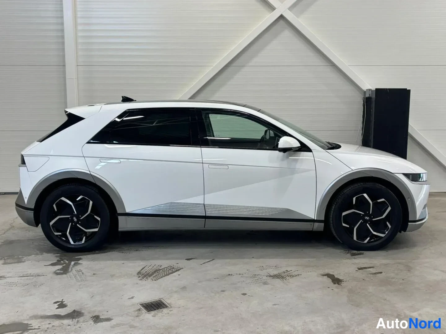 Sivulta: Hyundai Ioniq 5:n sivukuva oikealta; valkoinen kori, musta lasikatto ja kontrastinharmaat alatalat ja pyöränkaaret.