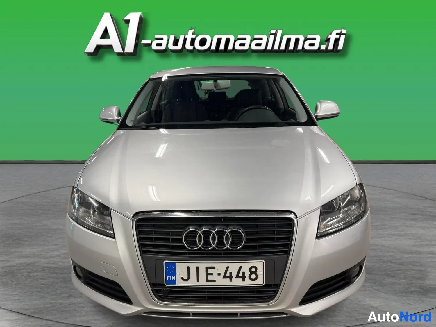 Edestä: Suoraan edestäpäin kuvattu hopeanvärinen Audi A3, jonka keulassa näkyy merkkiensä kämmenosa ja rekisterikilpi.