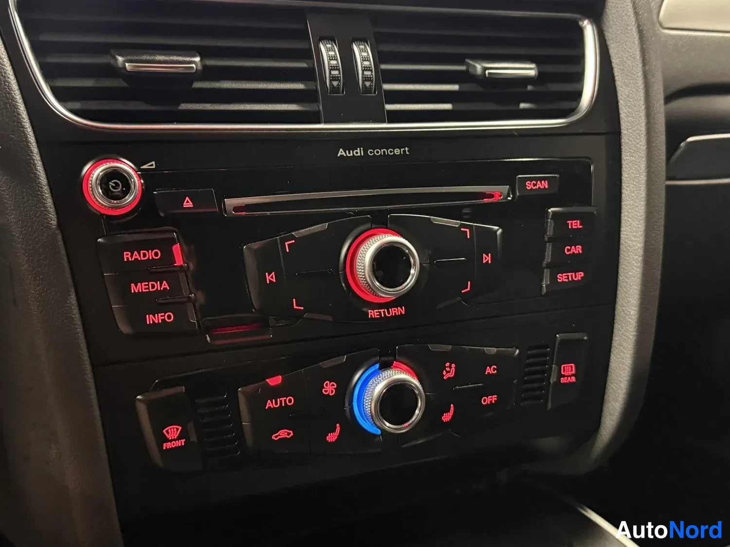 Yksityiskohta: Audi concert -radiolaite ja automaattinen ilmastointi, jossa näkyvät AUTO-, AC- ja OFF-napit, istuimenlämmittimen merkit sekä takalasin lämmitys.