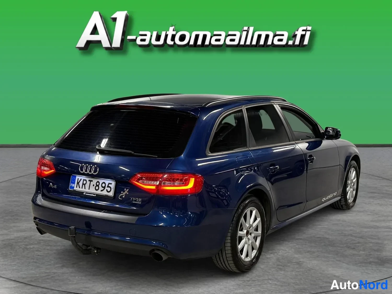 Takaviisto: Tummansininen Audi A4 Avant takaviistosta oikealta kuvattuna, kattotelineet, vetokoukku ja kaksoispakoputki näkyvissä.