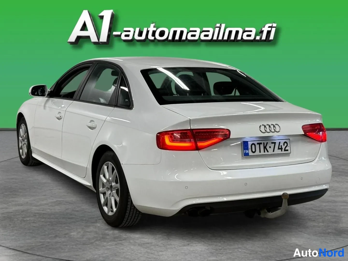 Takaviisto: Audi A4 Business 2,0 TDI 2012, takakulmakuva: valkoinen sedan, punaiset takavalot ja Audi-merkki/bootin kannella, rekisterikilpi, vasen sivu näkyvissä.