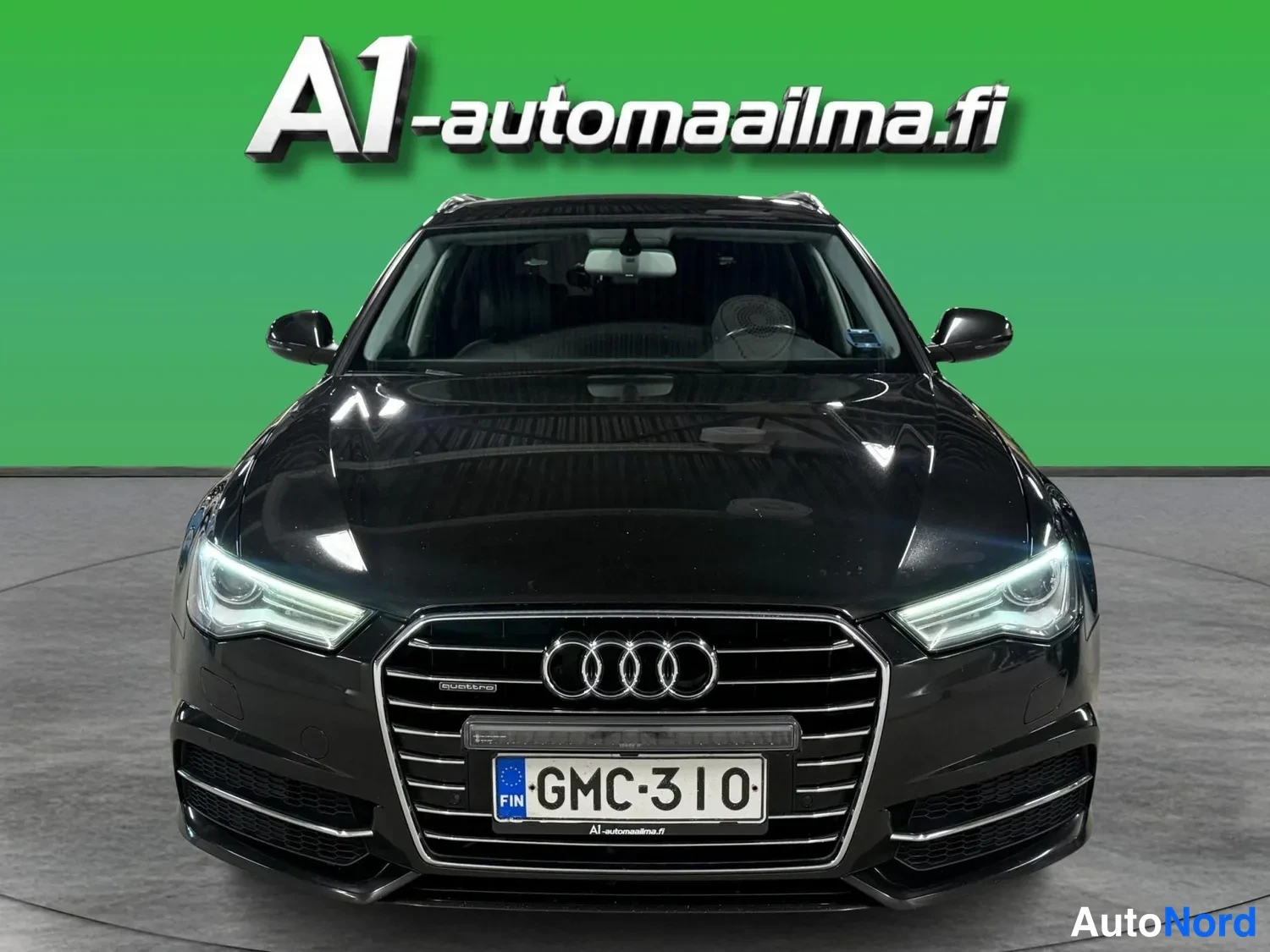 Edestä: Mustan Audi A6:n suora etukuva, etusäleikössä neljä renkaan merkkiä, rekisteritunnus.