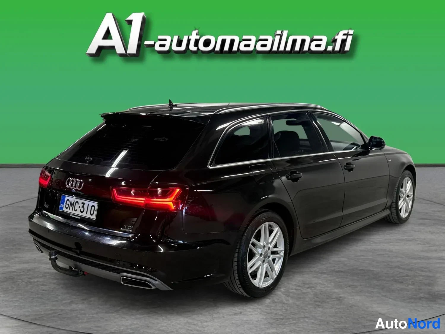 Takaviisto: Mustan Audi A6 Avantin takanurkkakuva vasemmalta, punaiset takavalot, rekisteritunnus ja vetokoukku näkyvät.