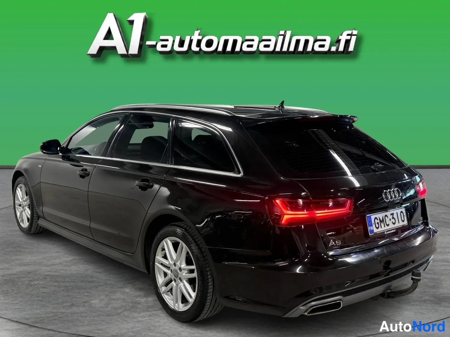 Takaviisto: Takakulmanäkyymä mustasta Audi A6 Avantista: yksi kylki ja takaosa kuvassa, rekisteritunnus, vetokoukku ja hopeiset kevytmetallivanteet.