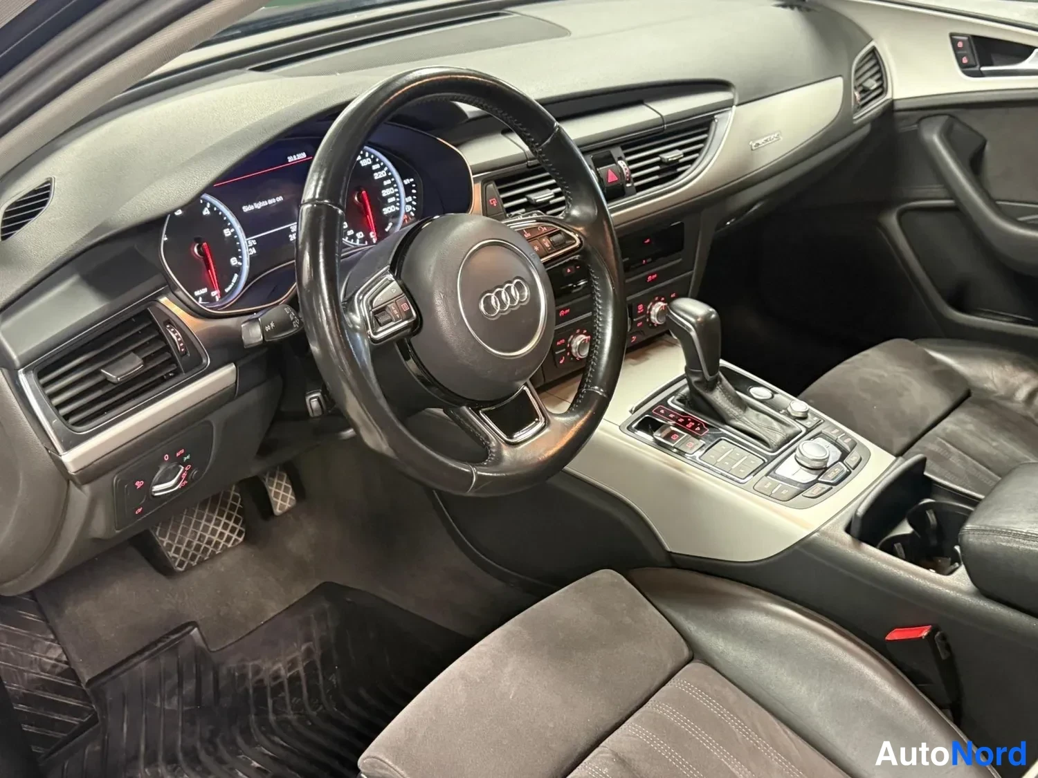 Muu: Autojen sisäkuva kuljettajan puolelta: Audi-ohjauspyörä, mittaristo, automaattivaihteen valitsin, keskikonsoli ja kankitakapenkin yläosa.