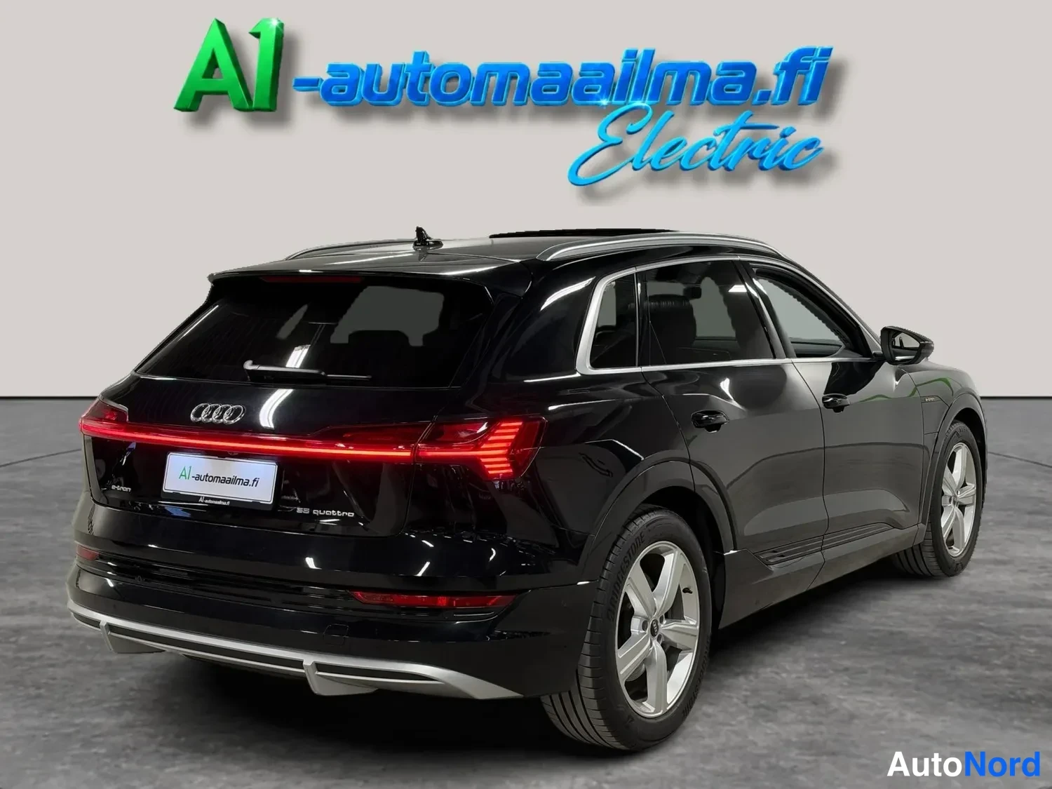 Takaviisto: Mustan Audi e-tron -maasturin takaosan kolmasosakuva, jossa näkyvät takavalot, teippaus A1-automaailma.fi ja hopeavanteet.