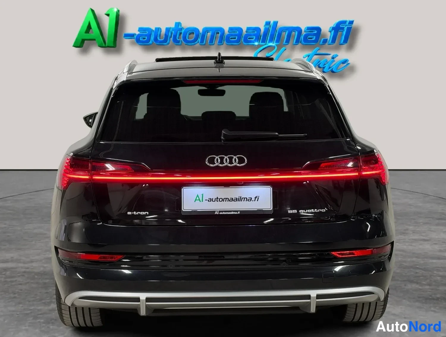Takaa: Mustan Audi e-tronin suora takanäkymä punaisella valoilmeellä ja A1-automaailma.fi -teippauksella.