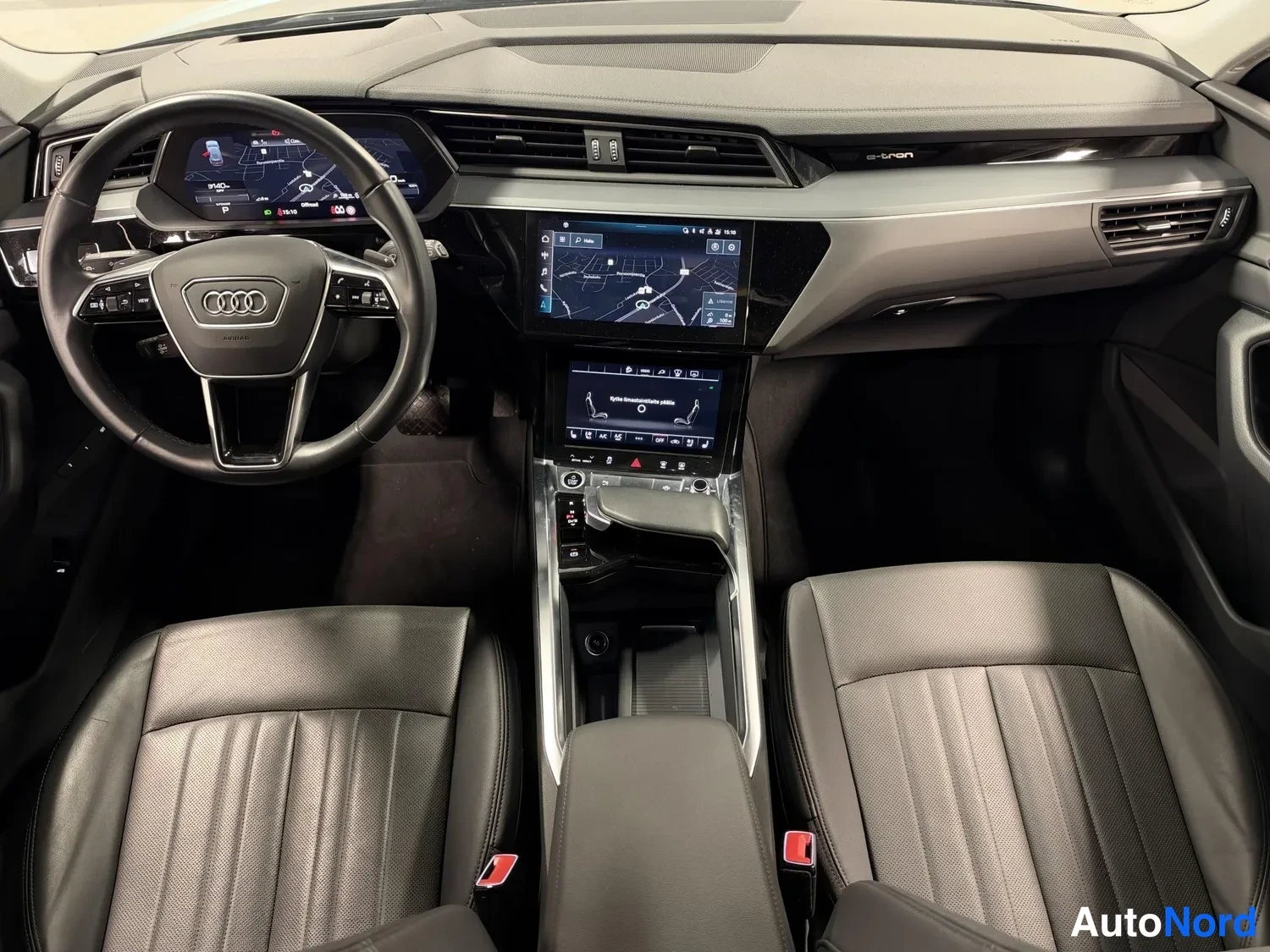 Muu: Audi e-tron -mallin matkustamo ylhäältä: mittaritaulu, keskinäytöt, ohjauspyörä ja kaksi mustaa nahkaistuinta.