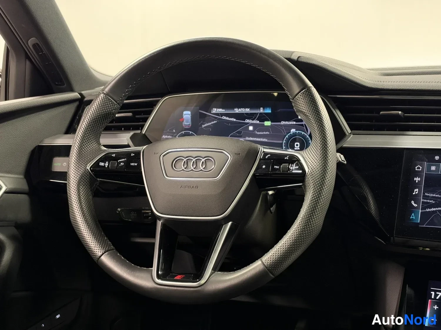 Muu: Lähikuva Audin monitoimiohjauspyörästä, AIRBAG-teksti ja Audi-merkki näkyvissä, takana virtuaalitörmämittaristo.
