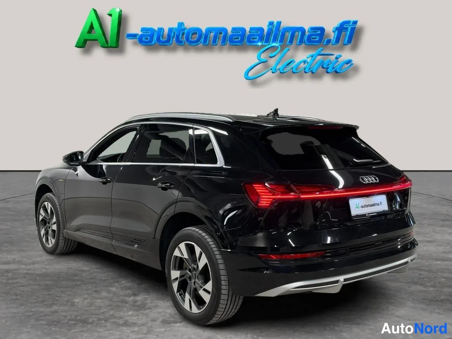 Takaviisto: Mustan Audi e-tronin taka-neljänneskuva, jossa näkyvät poikkileikkaava LED-takavalo, avattava takaluukku ja auton vasen sivu viisioväylillä.