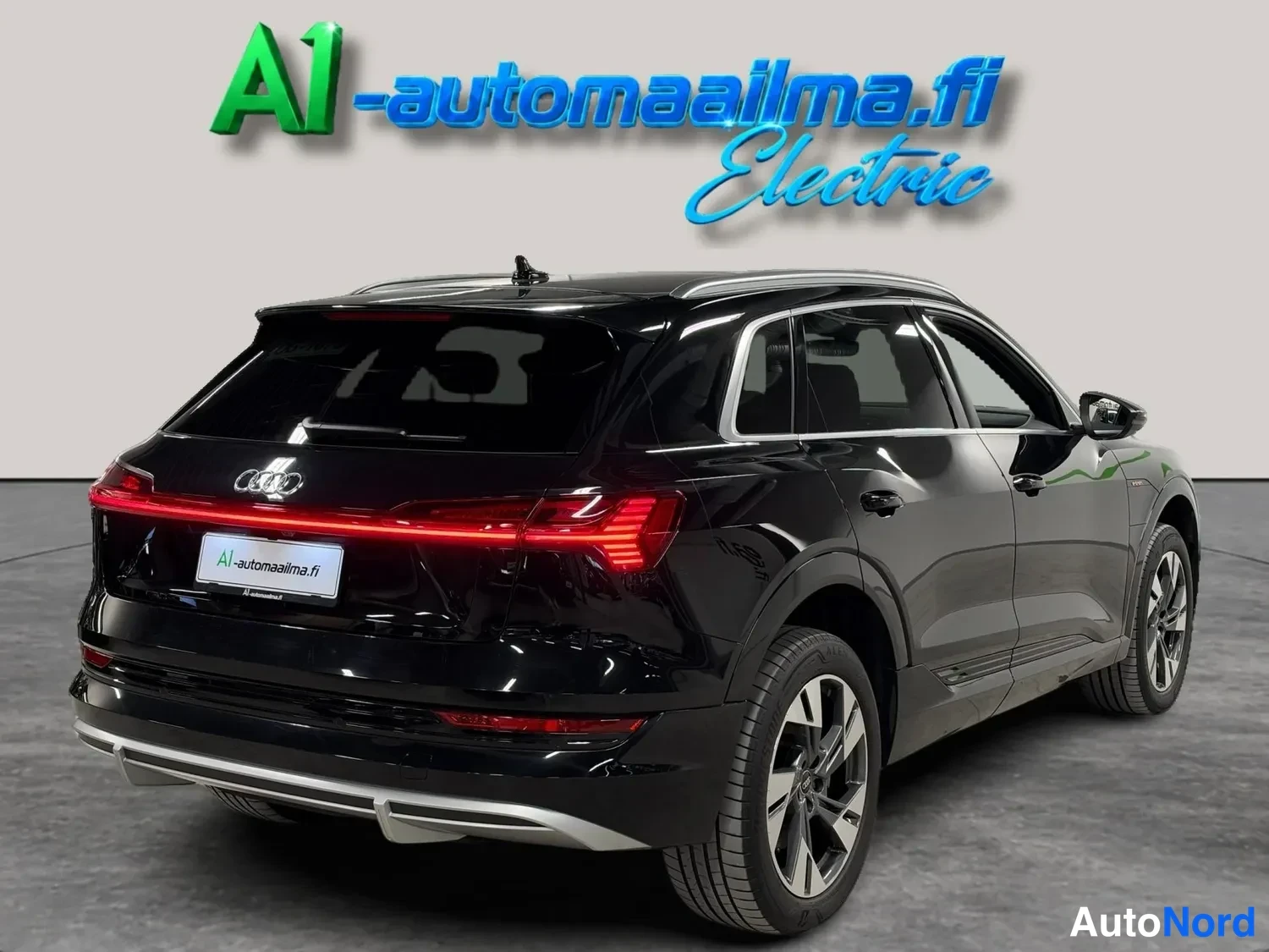 Takaviisto: Musta Audi e-tron kolmannesosan takakulmanäkymä: takanäyttö ja oikea kylki, hopeiset keransuojukset ja pölykuvat pyörät.