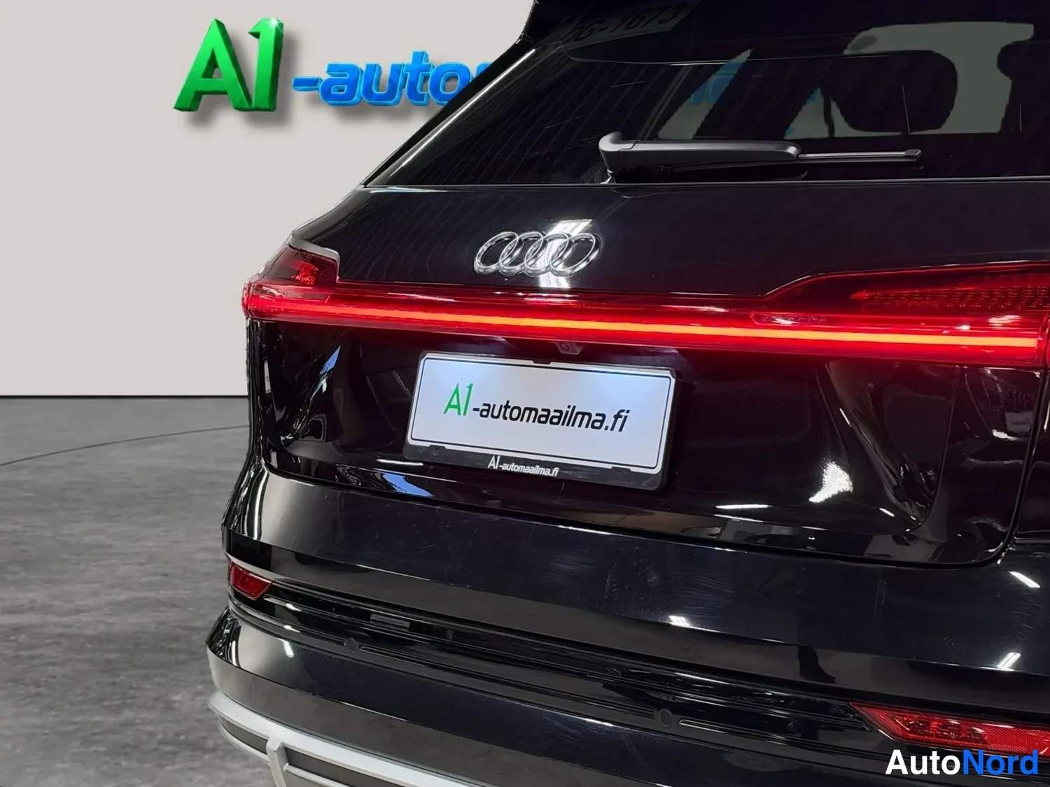 Takaa: Lähikuva mustan auton takapaneelista: Audi-merkki, punainen valojohto ja rekisterikilpi A1-automaailma.fi.