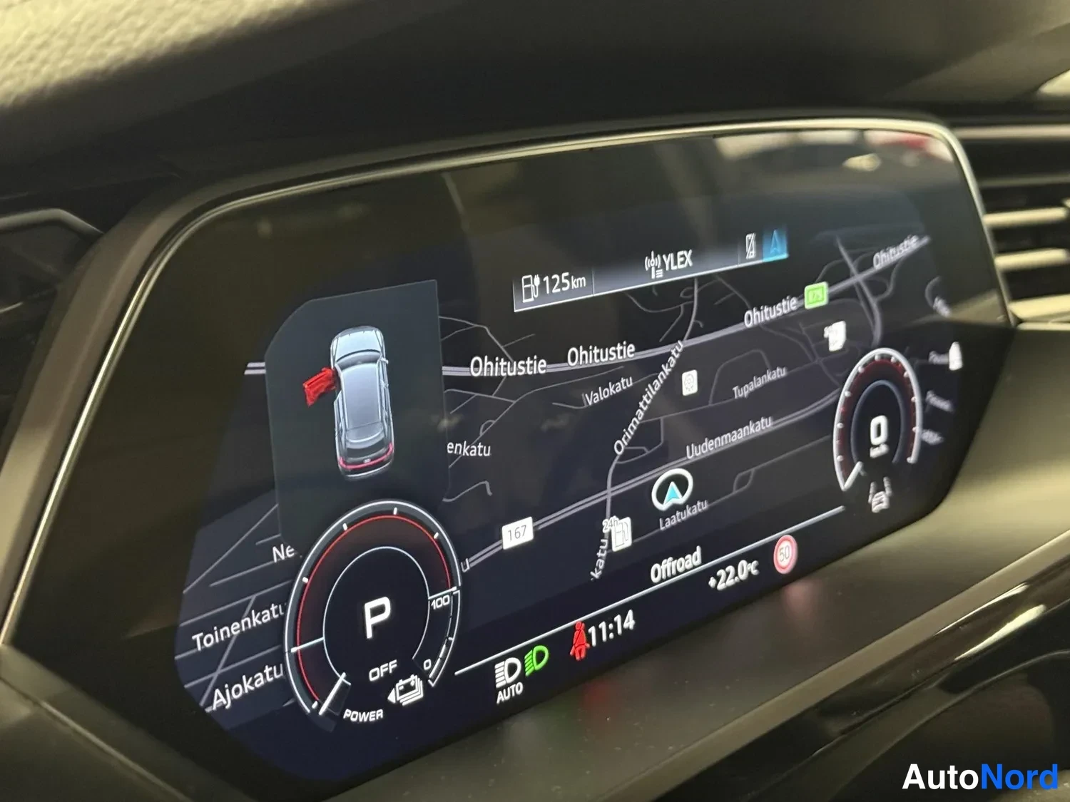 Muu: Audi e-tronin digitaalinen mittaristö näkyvissä: navigointikartta, seistova P-vaihde, 125 km toimintamatka ja YLEX-radiokanava.