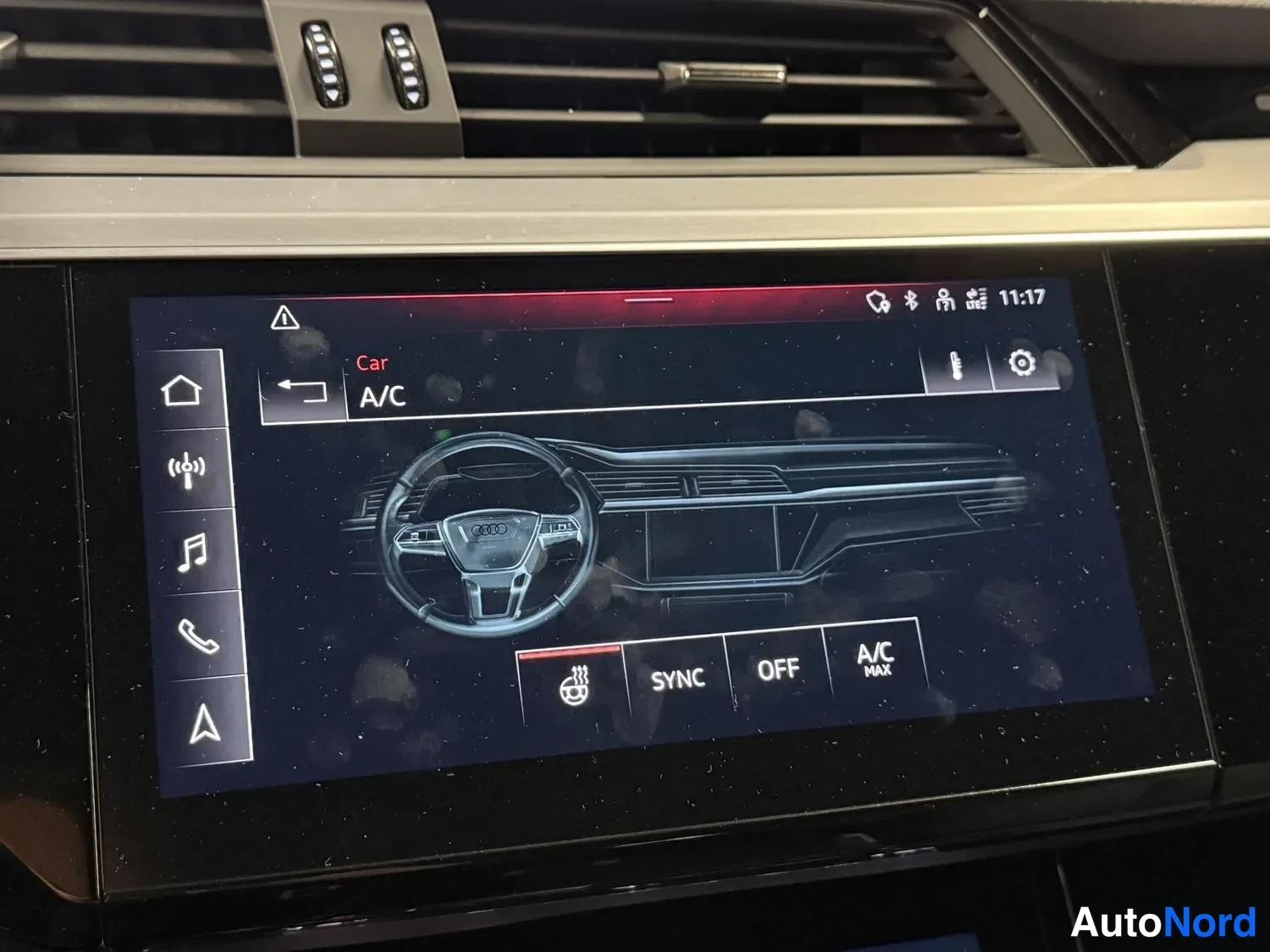 Yksityiskohta: Keskirivin näyttö Car/A/C-valikossa; A/C MAX, SYNC ja OFF-napit sekä Audi-logolla varustettu ohjauspyörän kuva.