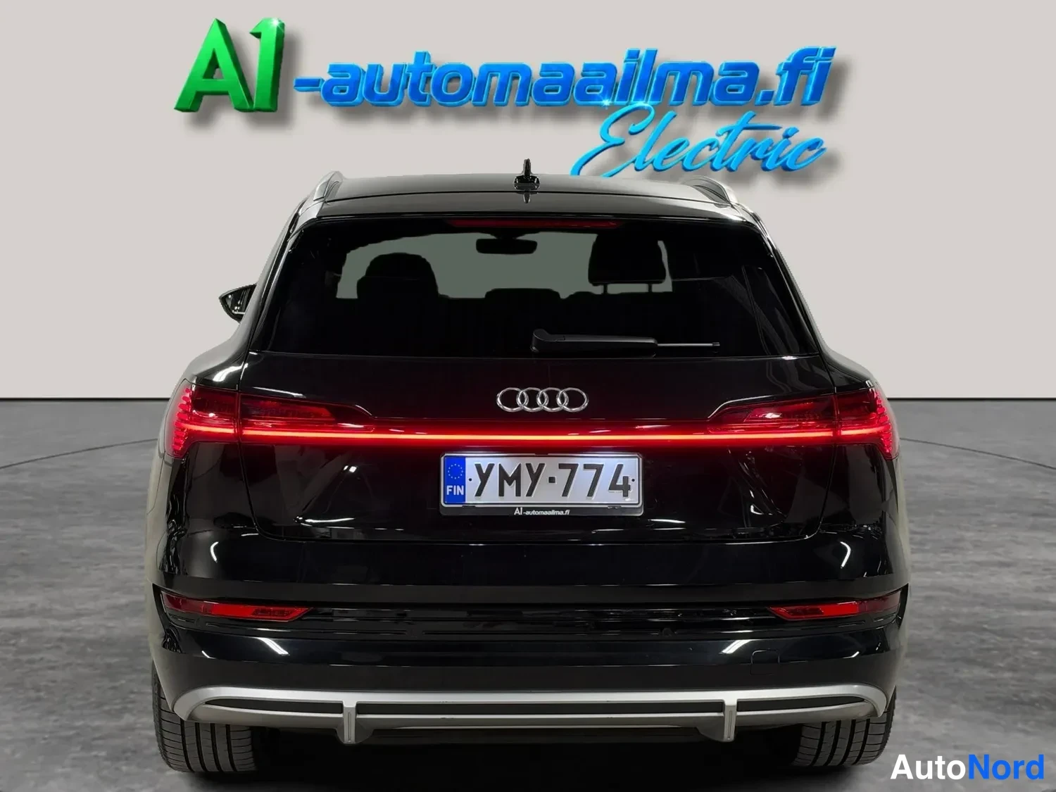 Takaa: Mustan Audi e-tronin takanäky, jossa näkyvät kk-merkkivalot, Audi-merkki ja rekisterikilpi.