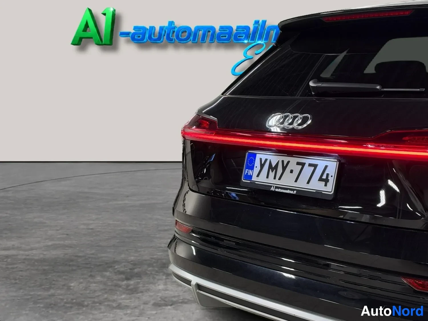 Takaa: Lähikuva mustan Audi e-tronin takapaneelista, kk-merkkivalot, Audi-merkki ja rekisterikilpi.