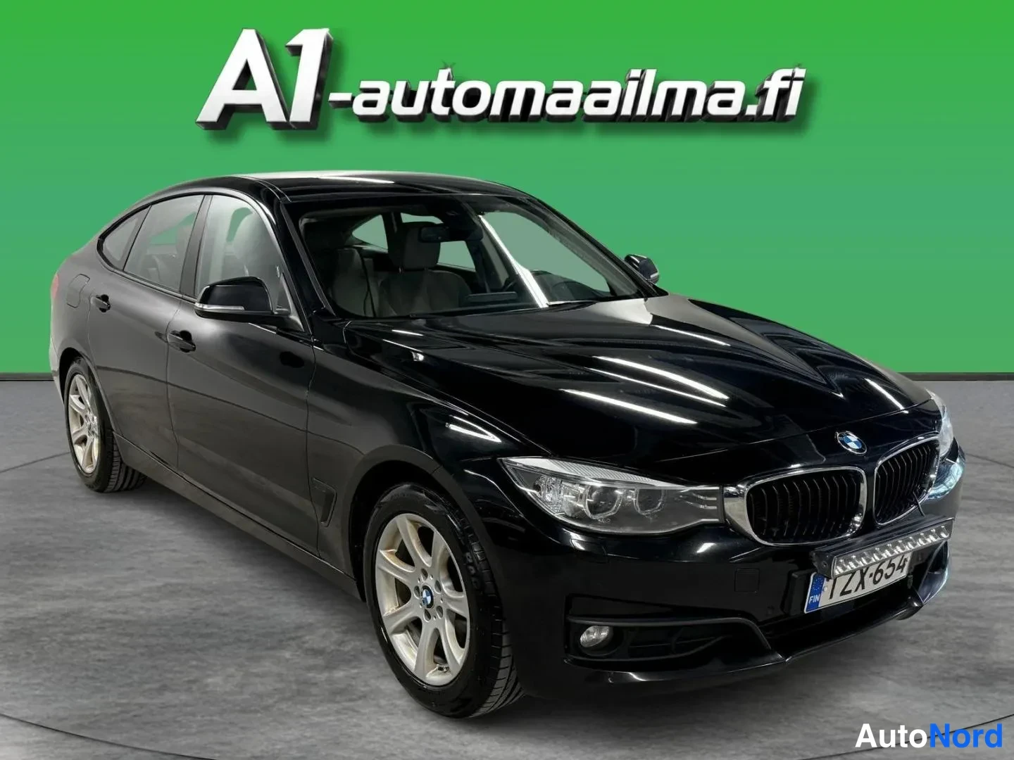 Etuviisto, nokka oikealle: Mustan BMW:n etukulmakuva oikealta, jossa näkyvät etusäleikkö, ajovalot, konepelti ja molempien ovien sivut vihreää taustaa vasten.