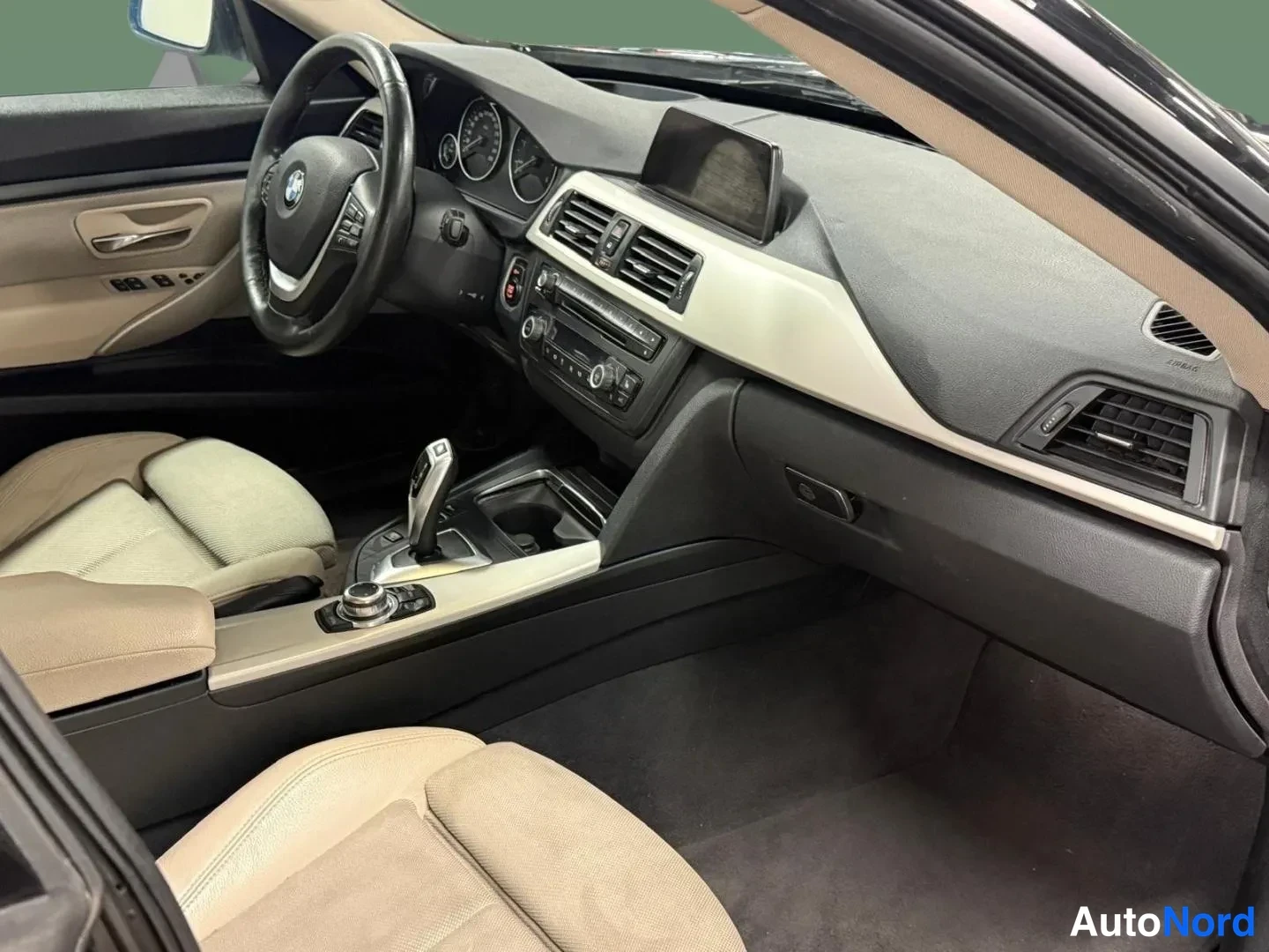Sivulta: Autojen sisätilakuva: BMW:n ohjaamo kuljettajan puolelta. Beige-punaiset istuimet, musta hansikaslokerikko, automaattivaihteiston valitsin ja iDrive-ohjain kesk