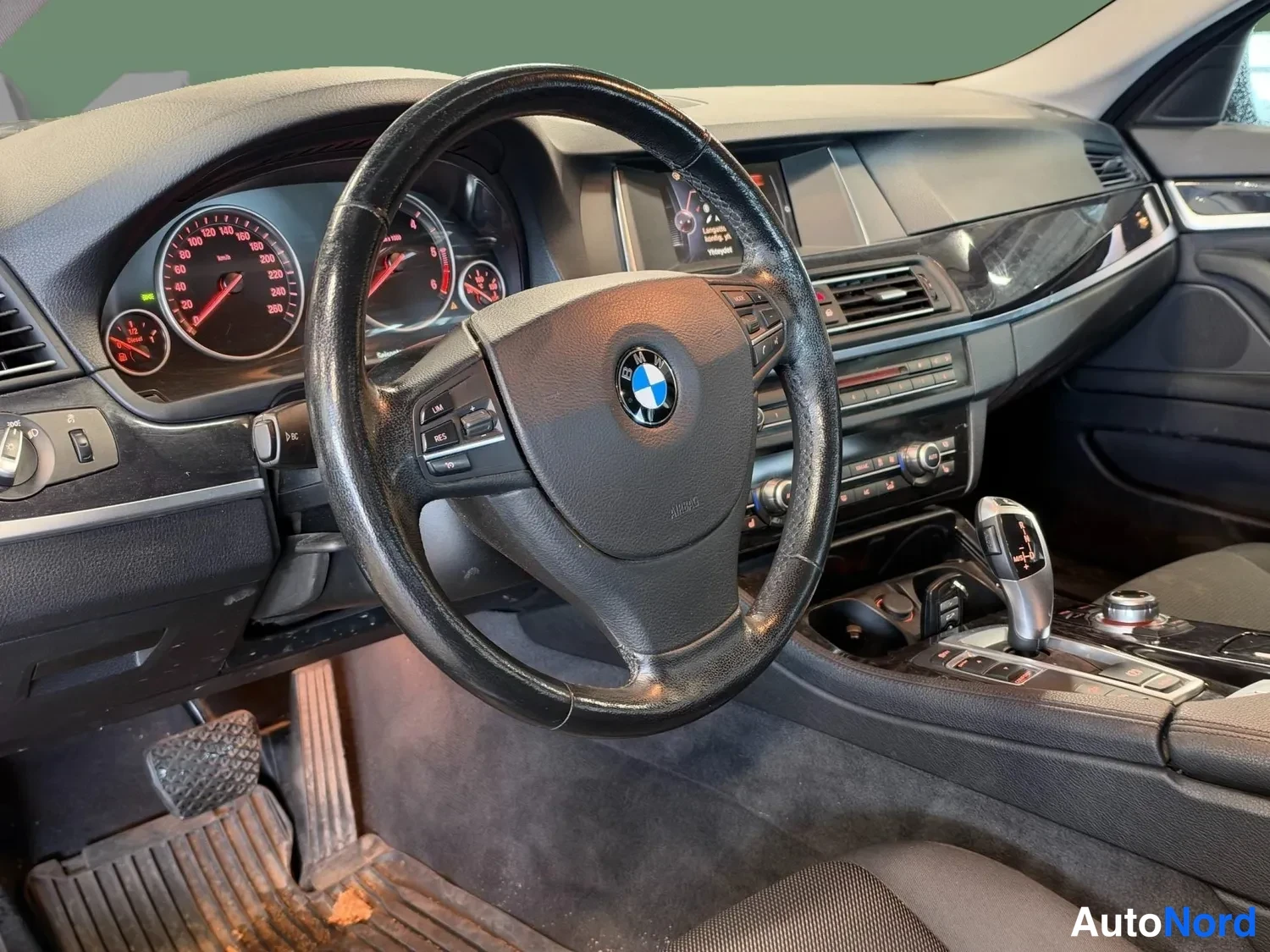 Sivulta: Kuljettajan paikasta kuvattu kojelauta: BMW-merkkinen ohjauspyörä, ympyrämittaristo, keskikäyttöpaneeli ja automaattivaihteen valitsin näkyvät.