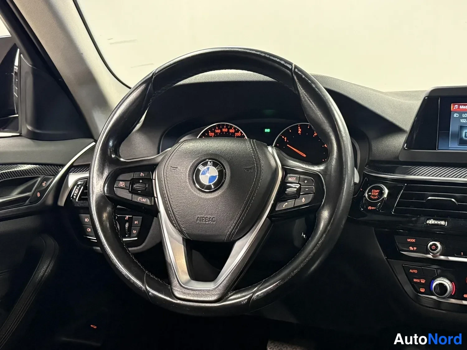 Edestä: Ohjauspyörä ja kojelauta. BMW-merkki ohjauspyörässä, mittaristo ja keskikonsolin näyttö näkyvät.