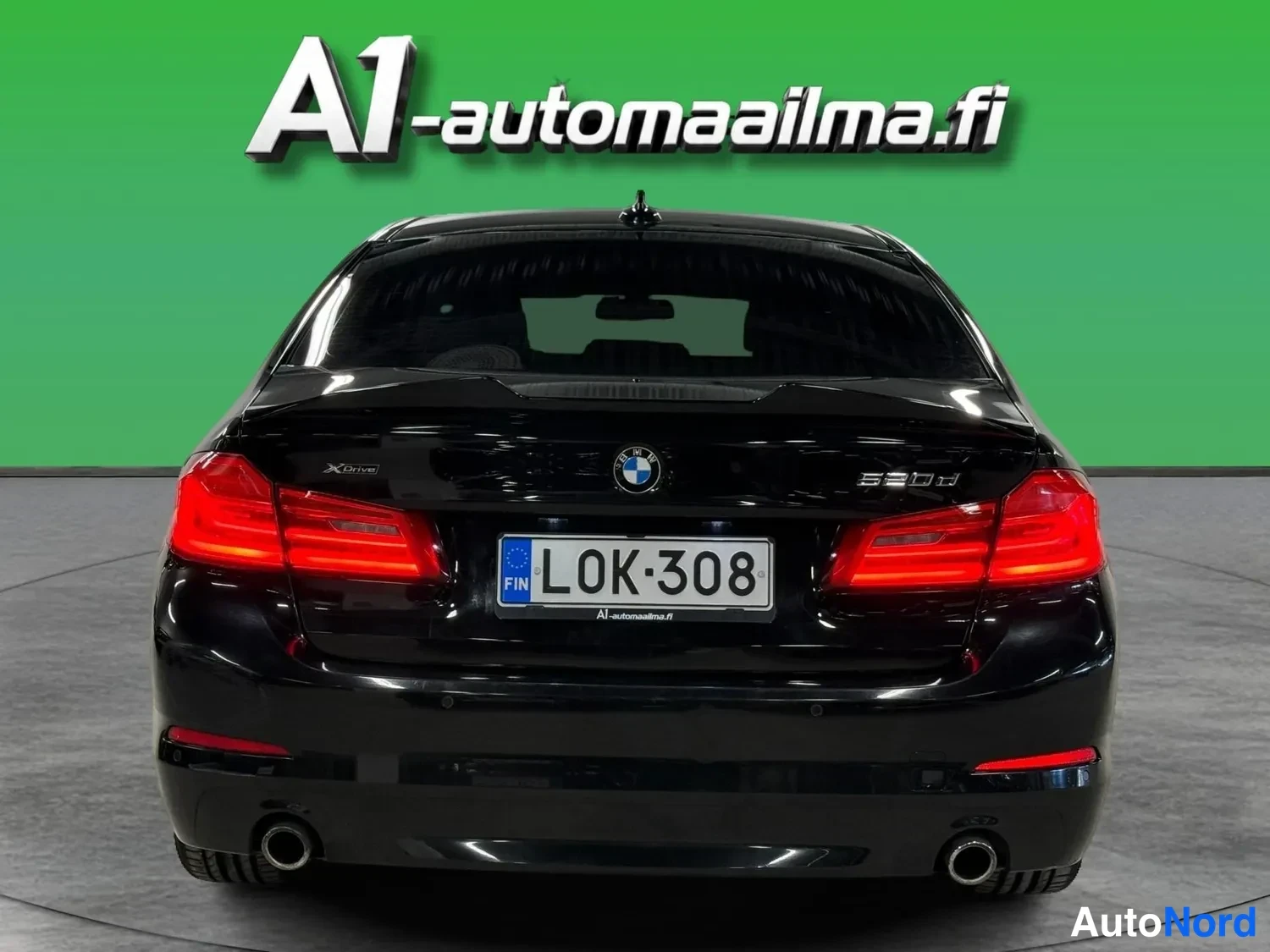 Takaa: Mustan sedanin takaosa suoraan takaa: punaiset takavalot, rekisterikilpi, BMW-merkki ja kaksi pakoputkea.