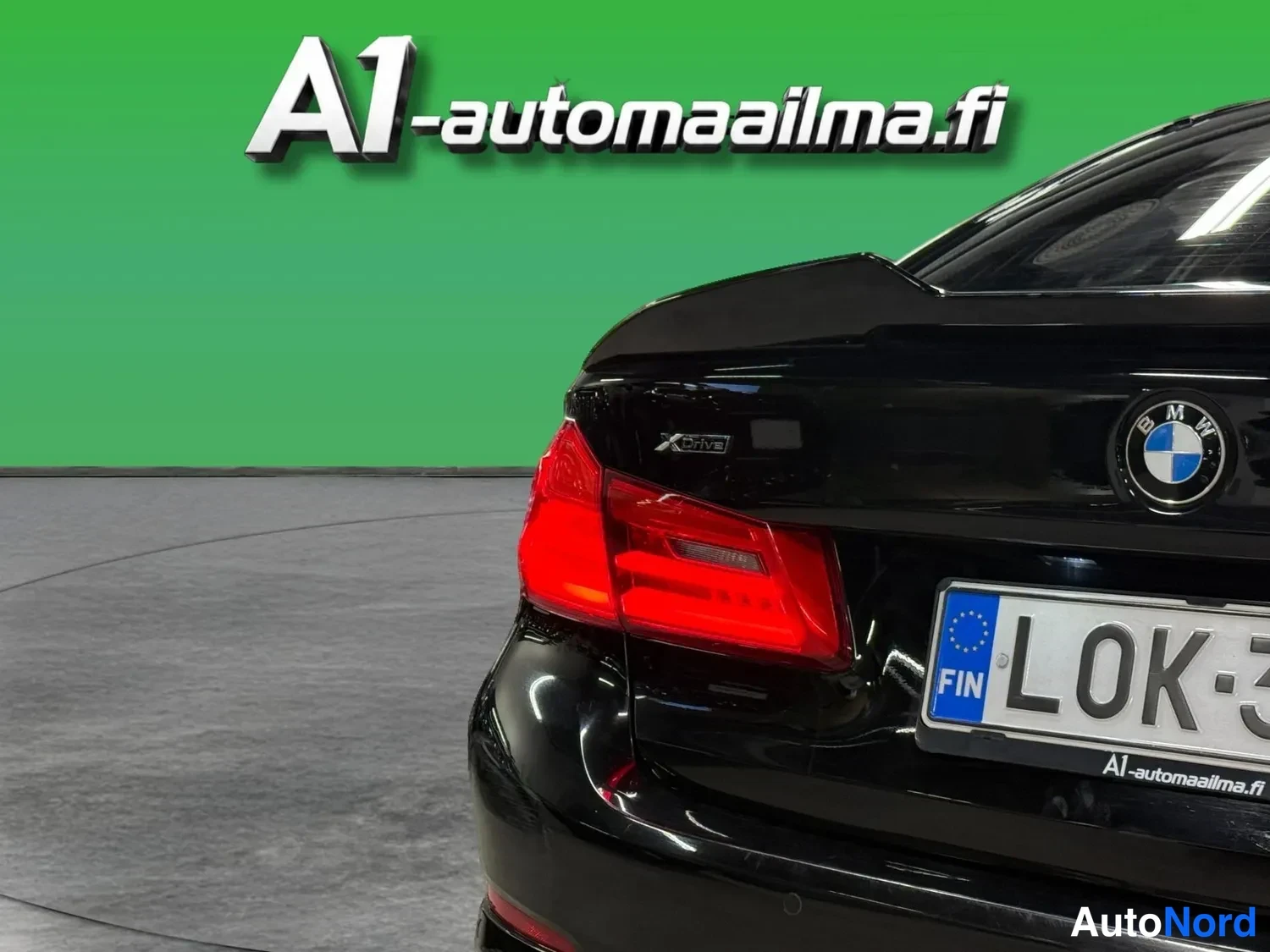 Takaa: Lähikuva mustan auton vasemmasta takanurkasta: punainen takavalo, BMW-merkki, xDrive-teksti ja osa rekisterikilvestä.