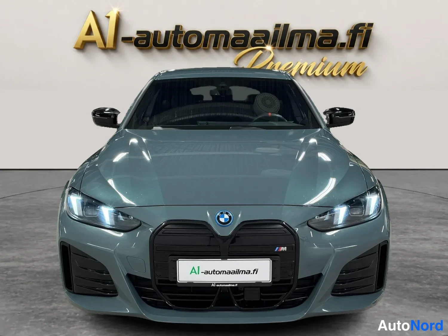 Edestä: BMW i4 suoraan edestä, harmaa kori, musta munuaissäleikkö ja M-merkki etupuskurin alueella.