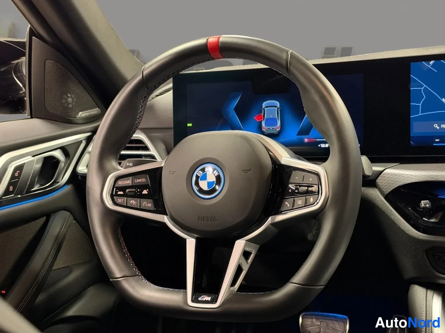 Muu: Ohjaamossa: BMW-ratin takaa näkyy kaareva näyttö, jolla on kartta- ja ajoneuvonäkymä.