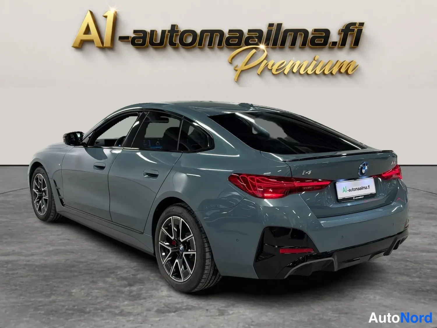 Takaviisto: BMW i4 takaviisto vasemmalta, harmaa korirunko, punaiset takavalot ja musta diffuusori näkyvissä.