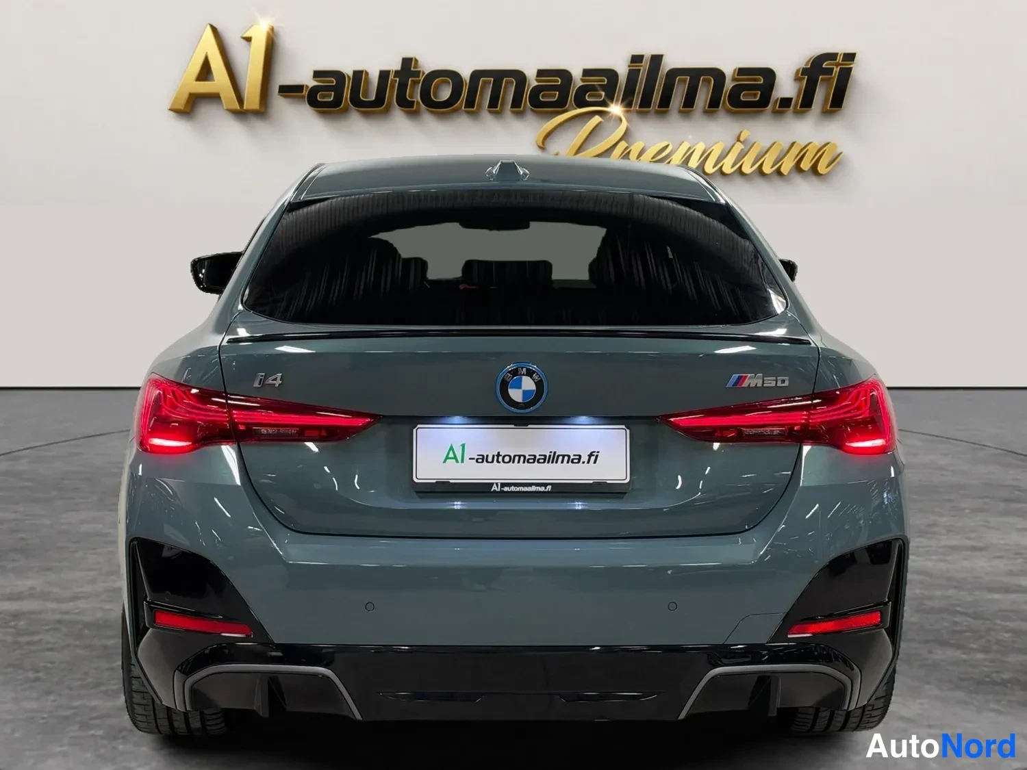 Takaa: BMW:n takaapäin otettu kuva, sinertävänharmaa koriväri, i4- ja M50-merkit sekä A1-automaailmatunnus näkyvät.