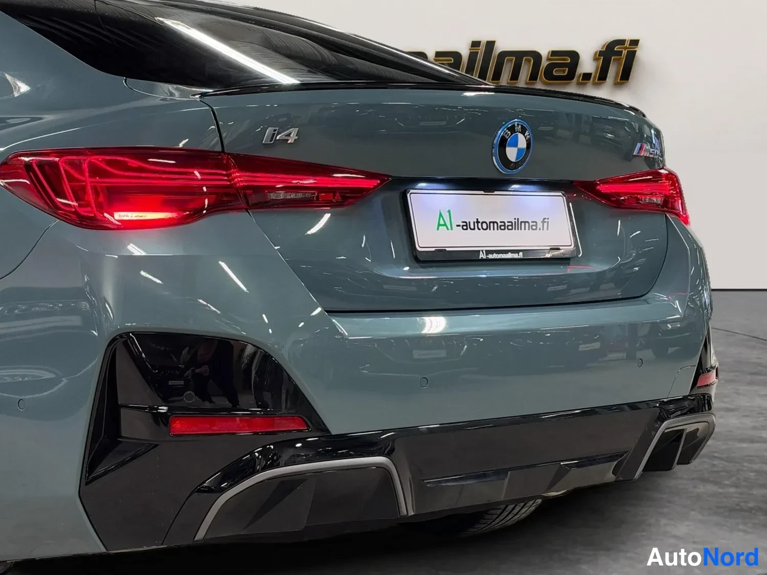 Takaa: BMW:n takaosa lähikuvassa, punaiset takavalot, i4-merkintä ja logo, tummanharmaa maali ja musta difformeri.