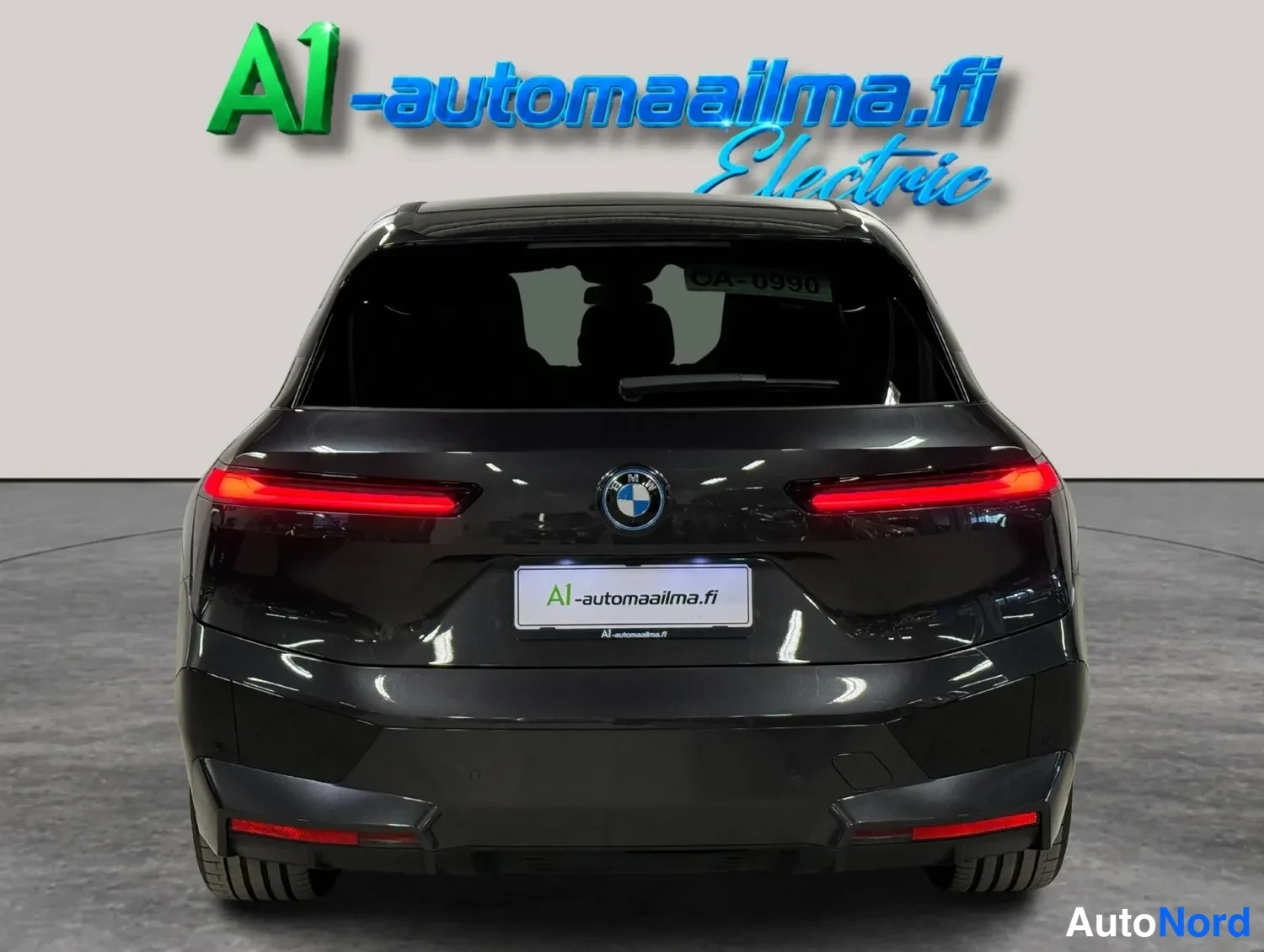 Takaa: Auton takapää suoraan takaa: tumma BMW-katemaasturi, punaiset takavalot ja A1-automaaailma.fi-kyltti rekisterikilven paikalla.