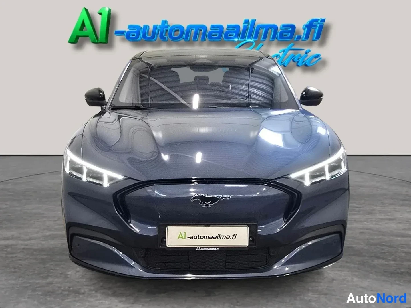 Edestä: Tummansinisen Ford Mustang Mach-E:n etupää suoraan edestä, etumoottorit ja Ford-merkki näkyvissä.