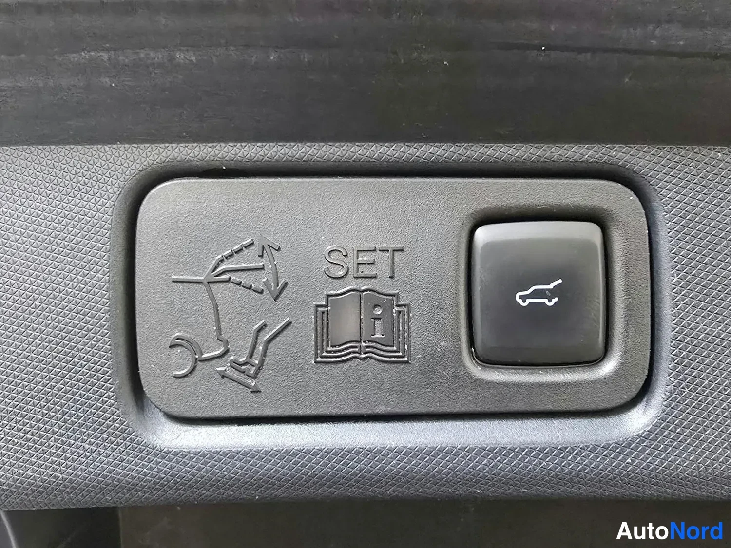 Yksityiskohta: Takaoven säädettävä istuimen nappi SET-tekstillä ja auto-symbolilla.