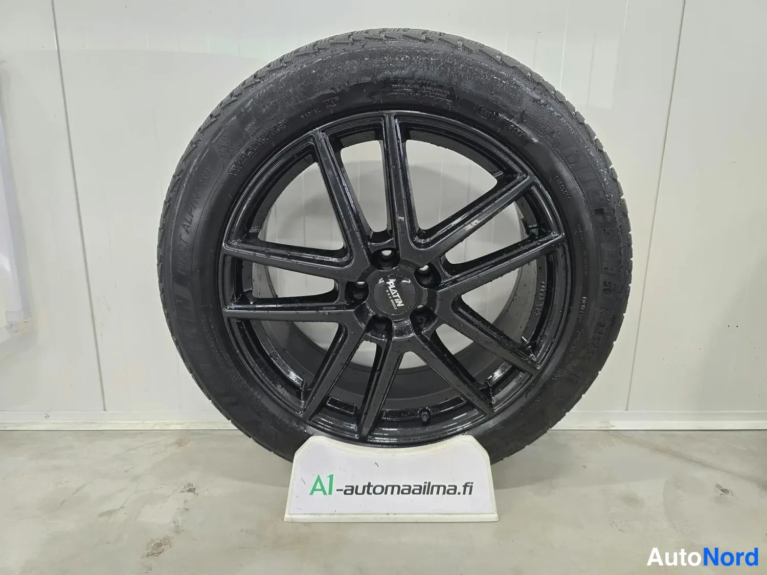 Yksityiskohta: Musta alumiinivanne Michelin-renkaalla esitteellä, jonka tekstinä A1-automaa1ma.fi.