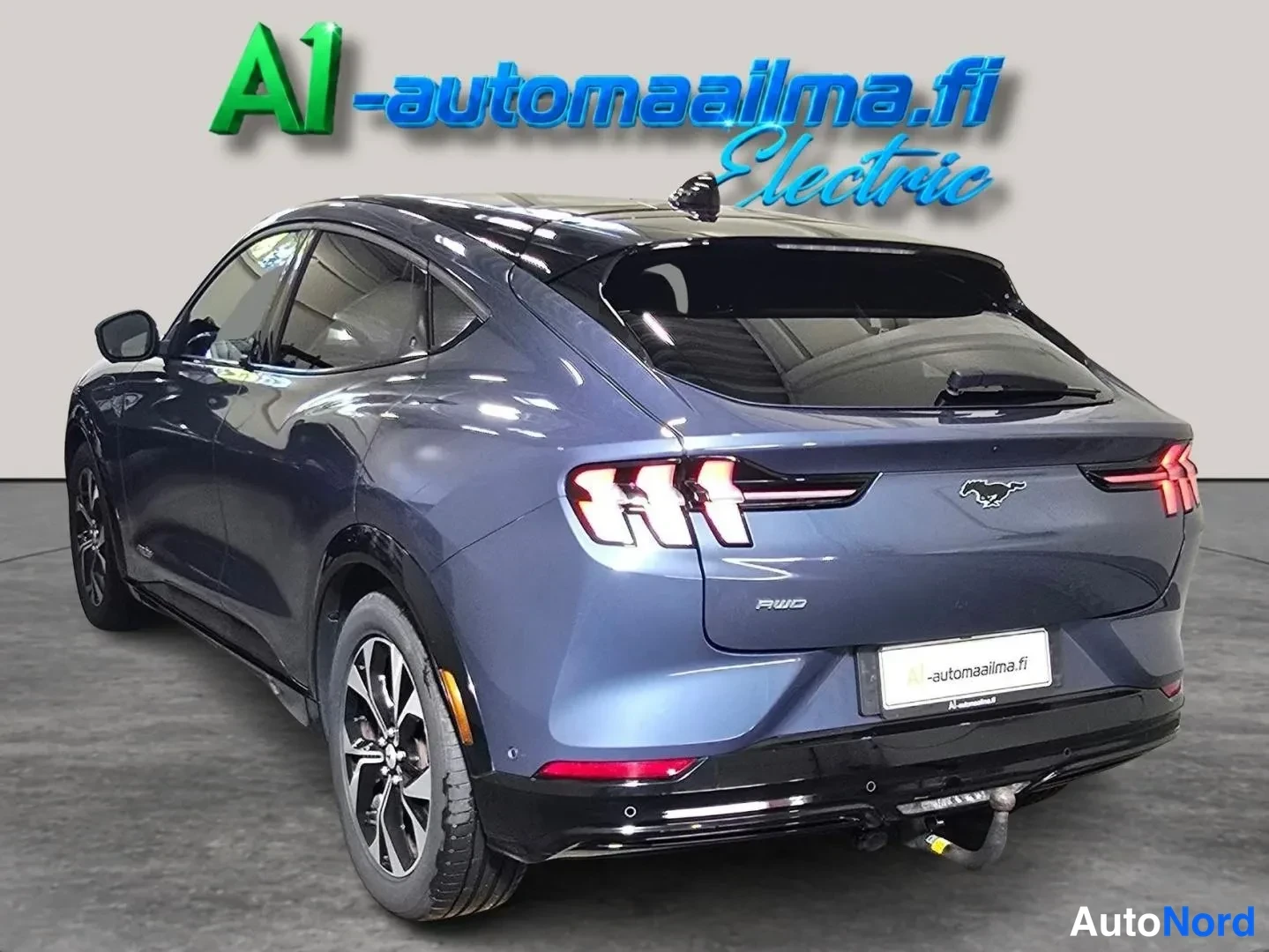 Takaviisto: Tummansinisen Ford Mustang Mach-E:n takakulma vasemmalta, perä ja kylki näkyvissä; lukko perään kytketty vetokoukku.