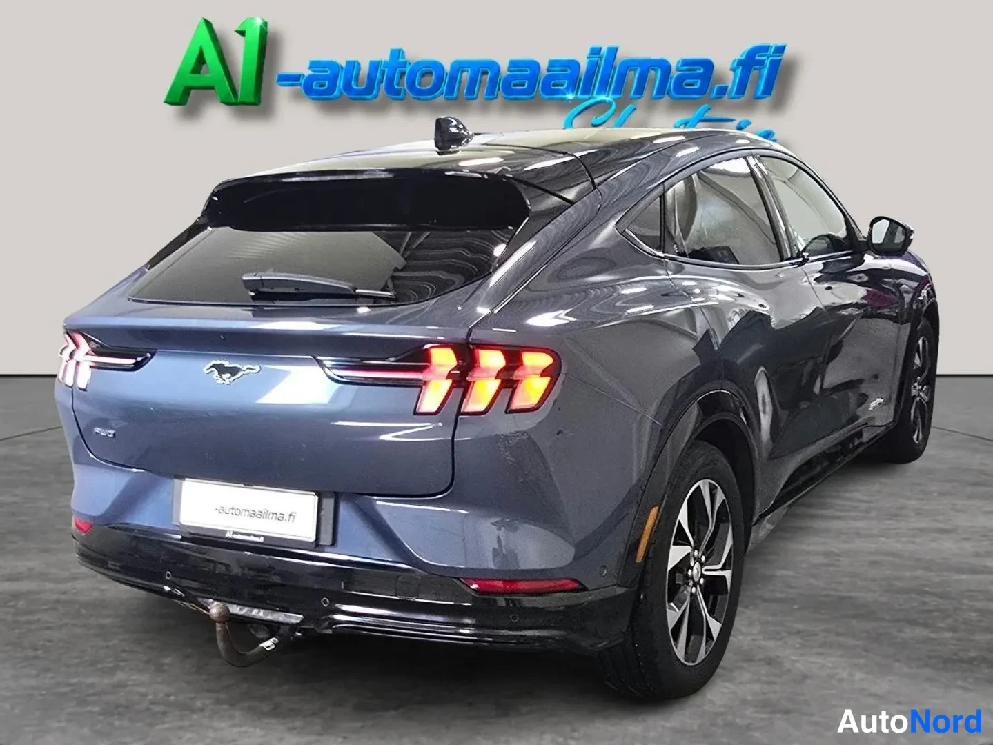 Takaviisto: Sinertävän harmaa Ford Mustang Mach-E takaa kolmesta neljänneksestä nähtynä, musta lasikatto ja perävaunukoukku näkyvissä.