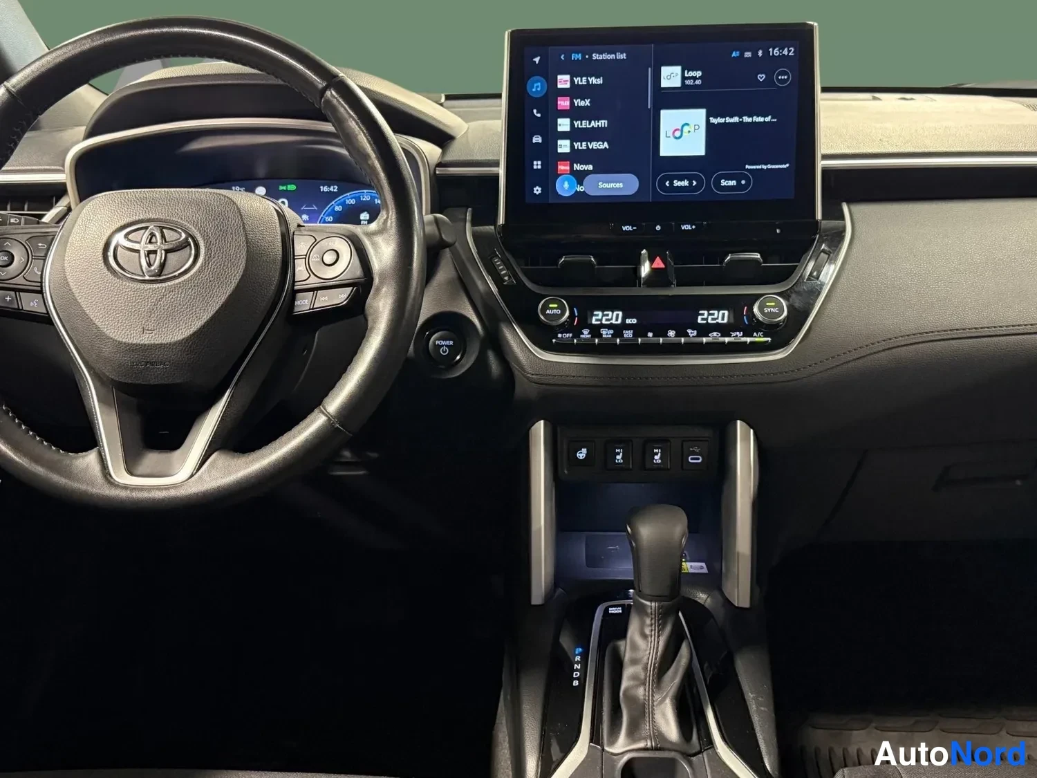 Edestä: Ohjaamo Toyota-merkillä: ohjauspyörä, kosketusnäyttö radio-sovelluksella (Yle-kanavat näkyvissä), kaksivyöhykeilmastointi 220/220, vaihteenvalitsin ja keskikons