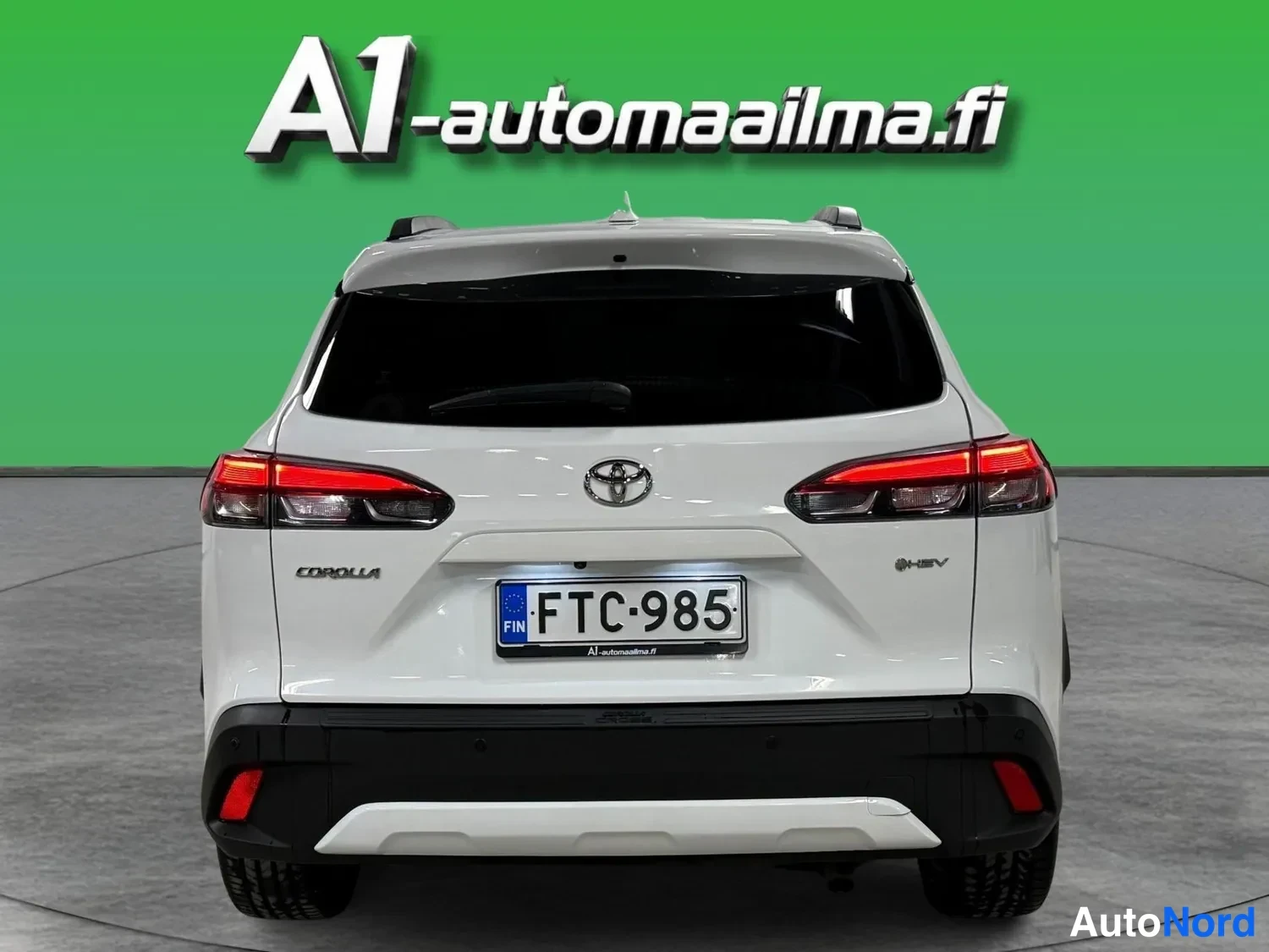 Takaa: Toyota Corolla Crossin takaosa suoraan takaa; valkoinen korimuovi, Toyota-merkki ja COROLLA-teksti, rekisteritunnus, mustat puskurit ja punaiset takavalot.